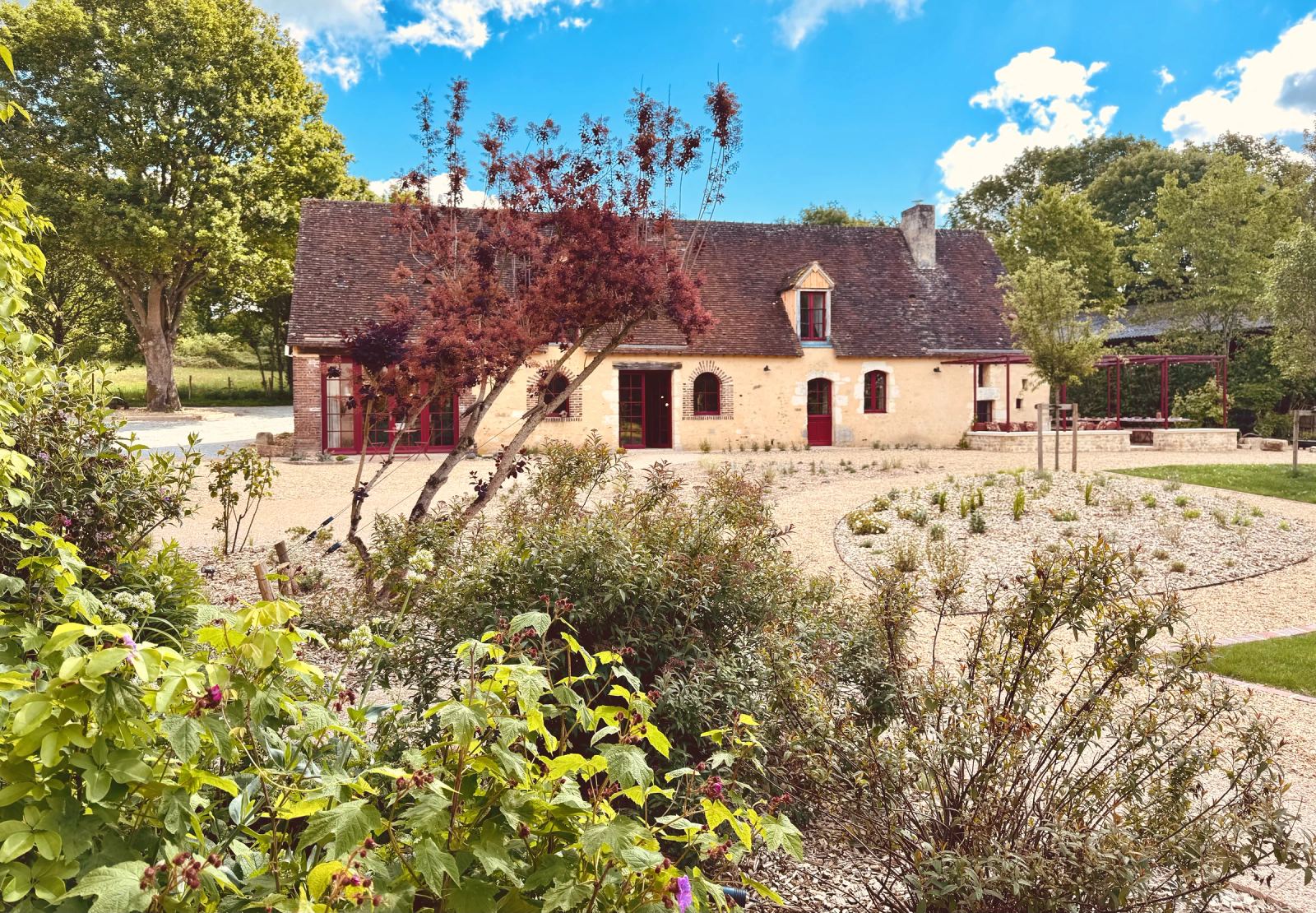 Façade en pierre et volets rouges de la maison principale, cour gravillonnée et massifs — Maison Oiserie