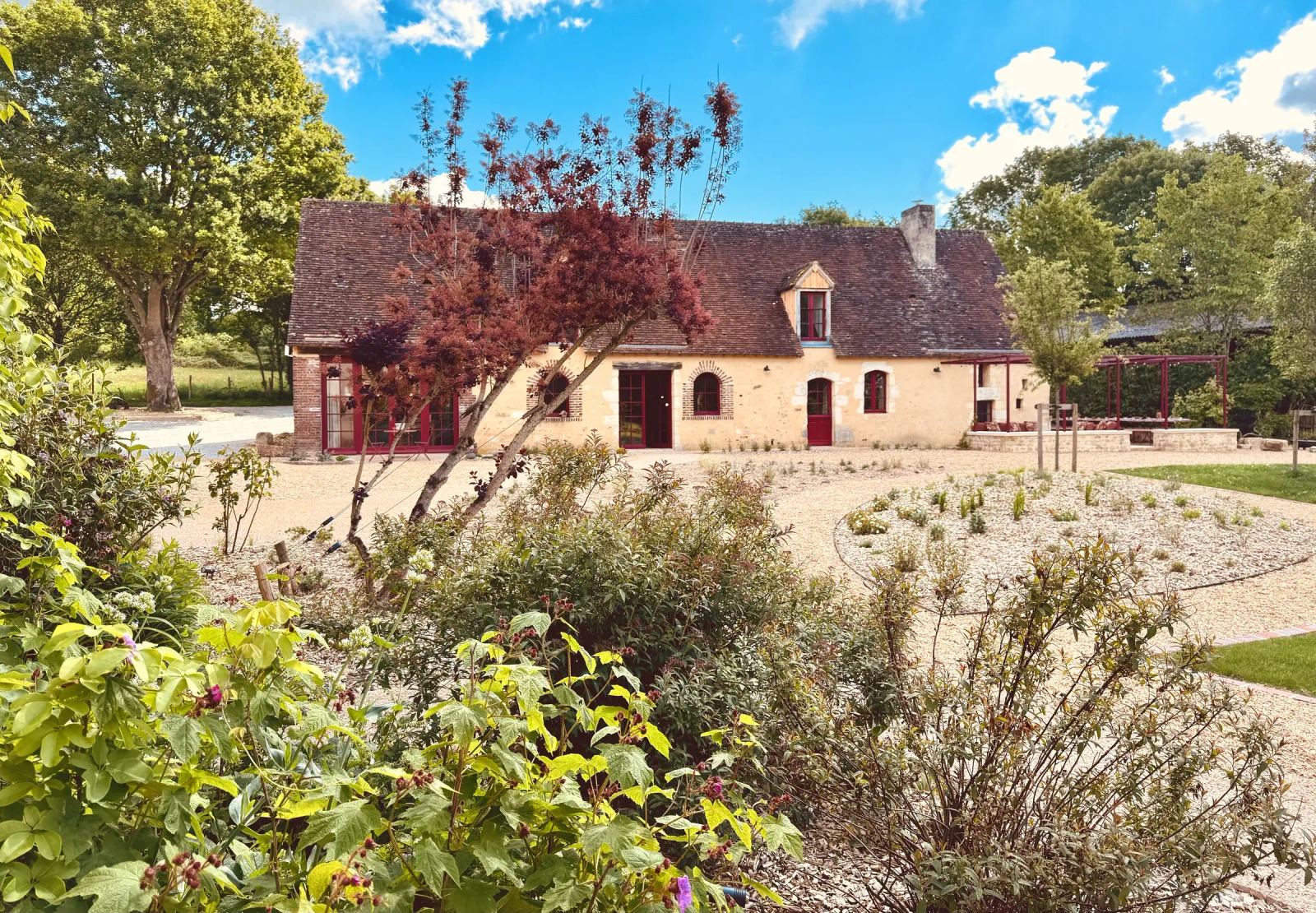 Façade en pierre et volets rouges de la maison principale, cour gravillonnée et massifs — Maison Oiserie