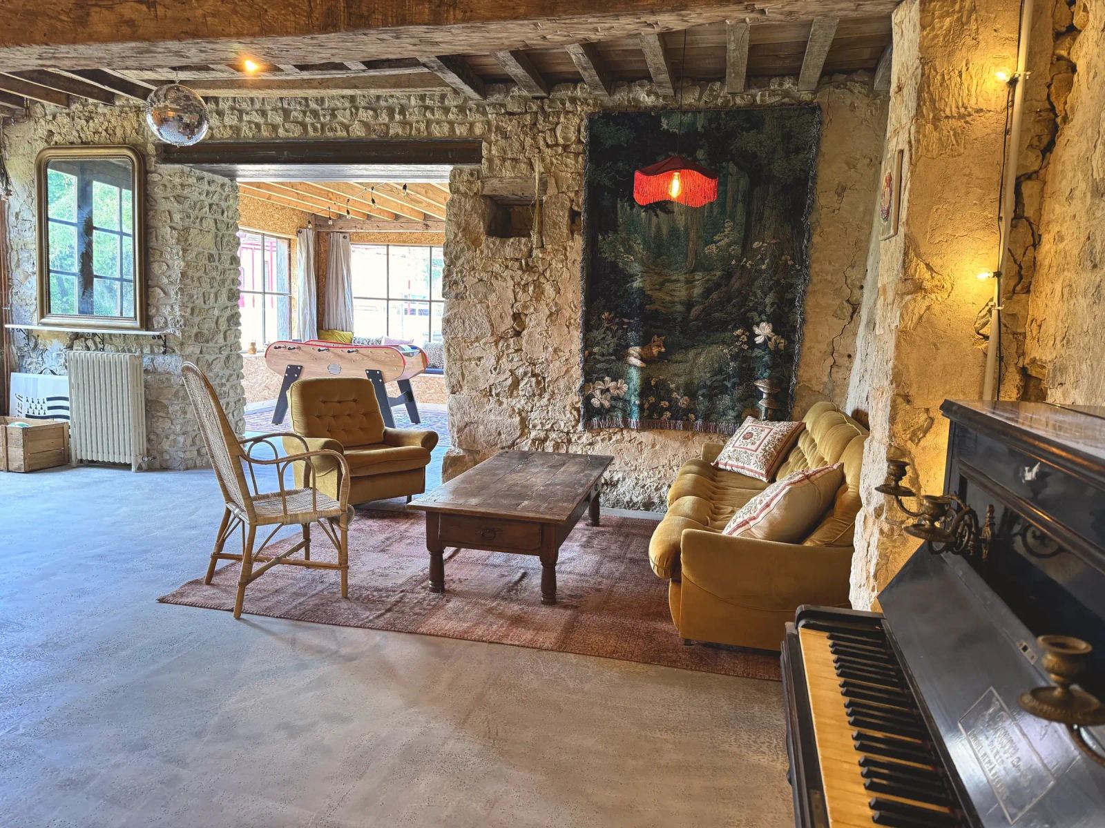 Salle de jeux et salon aux murs de pierre, fauteuils, piano et vue sur le jardin d'hiver — Maison Oiserie